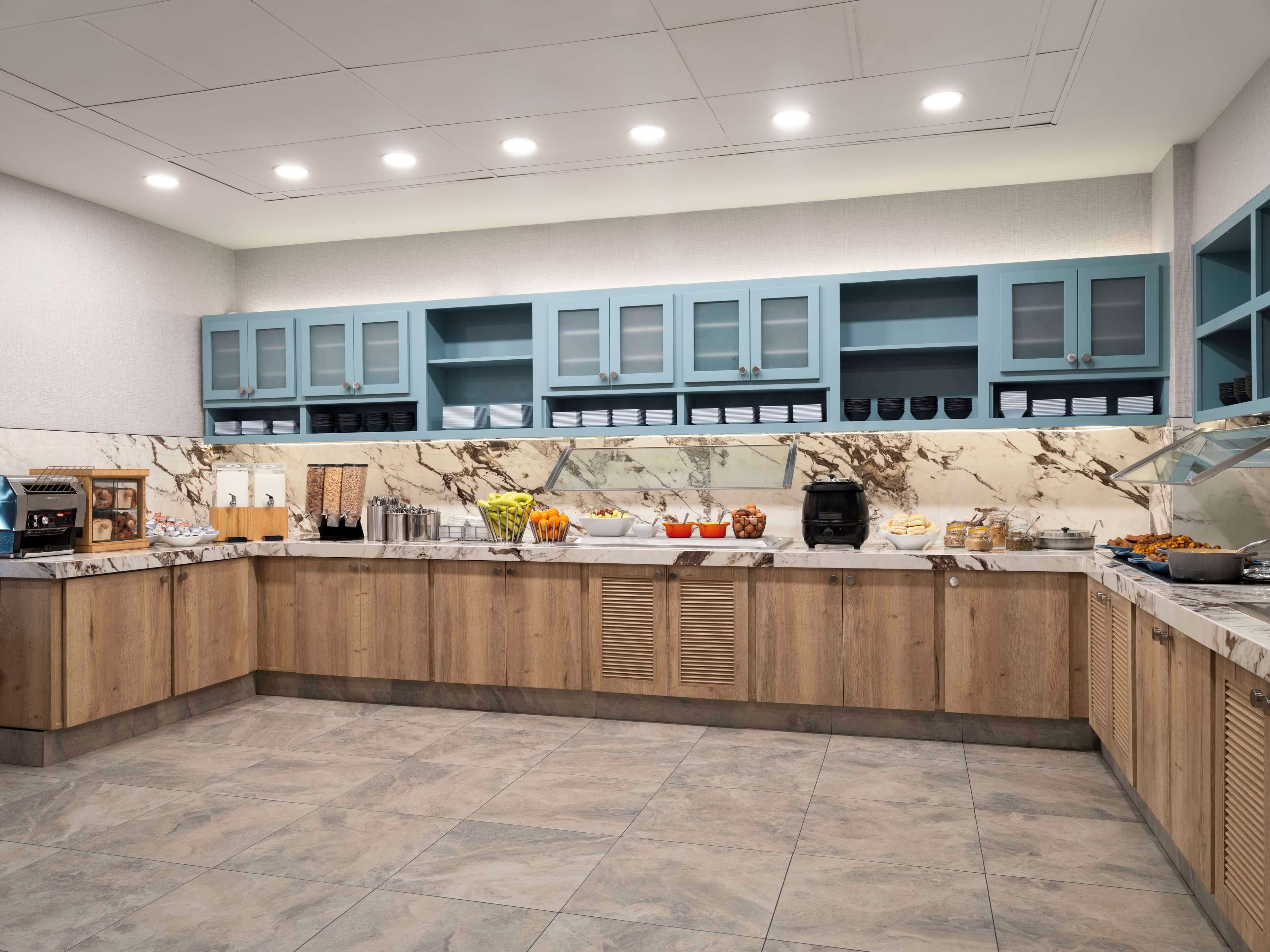 A modern kitchen with marble countertops, wooden cabinets, and blue upper cabinets.
