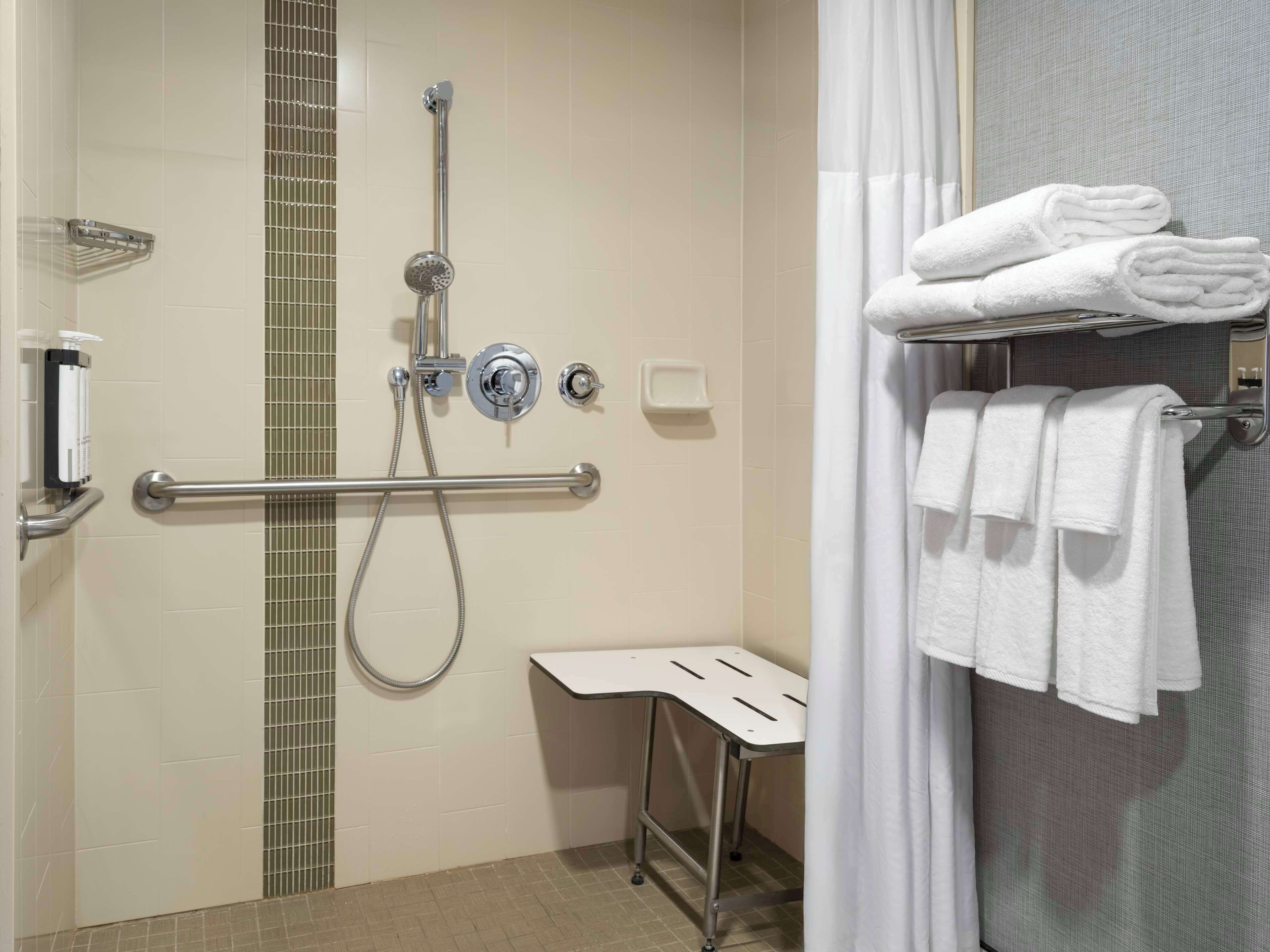 A bathroom with a shower, grab bars, a towel rack, and a soap dispenser.