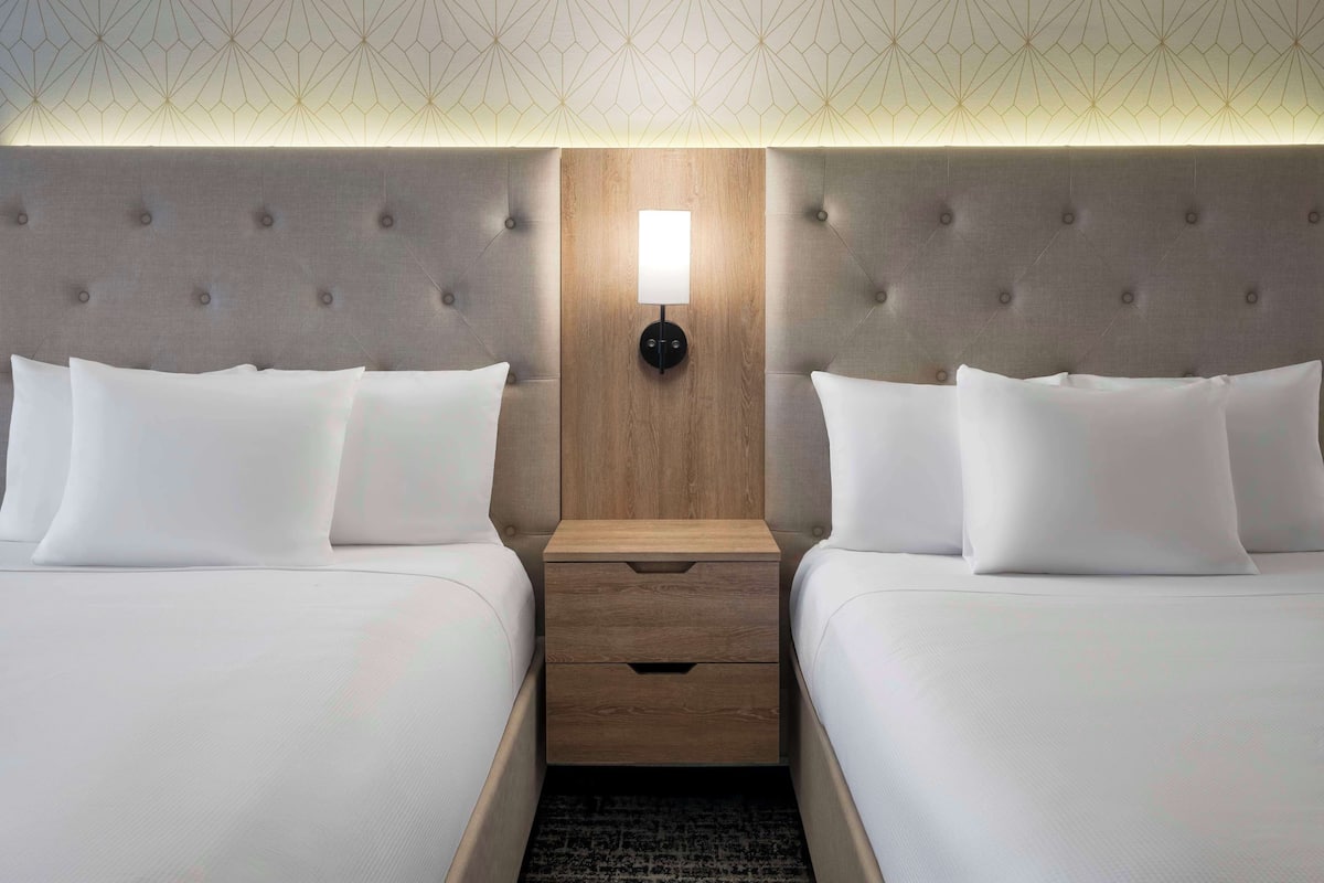 A hotel room with two beds, a wooden headboard, a nightstand with a lamp, and a patterned ceiling.