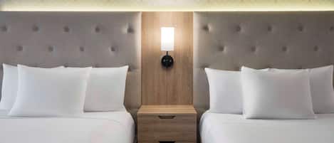 Habitación de hotel con dos camas, cabecero de madera, mesita de noche con lámpara y techo estampado.