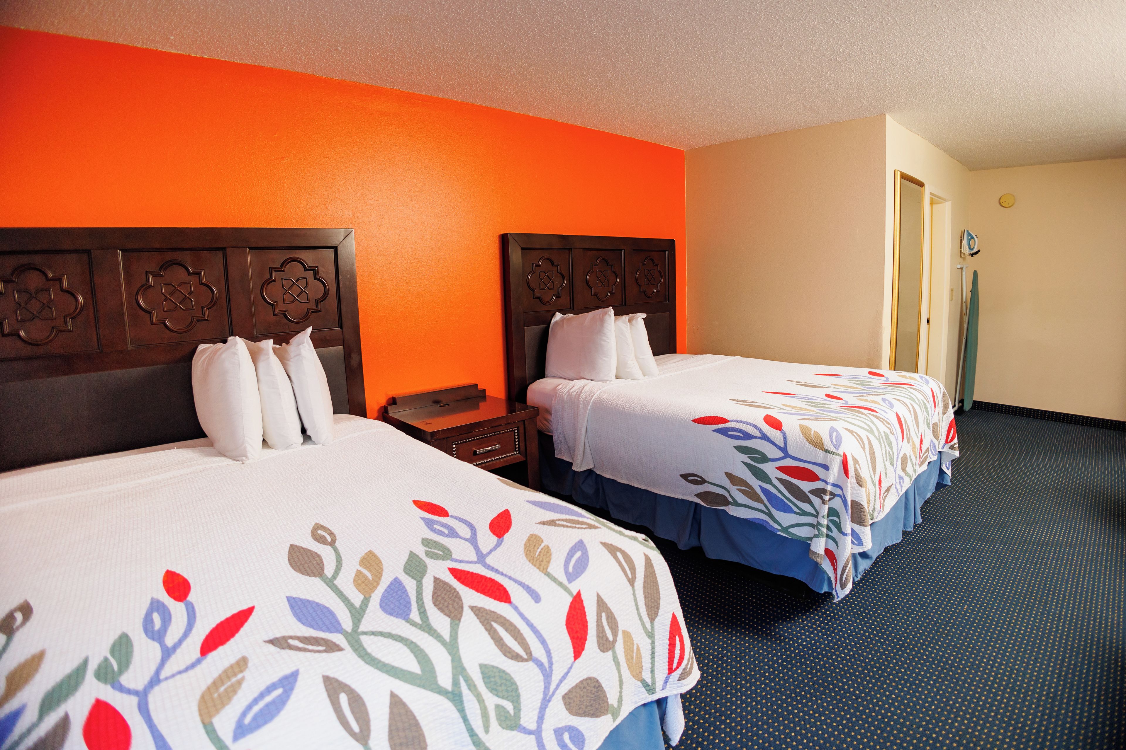 A hotel room with two beds, each with a floral-patterned bedspread, a wooden headboard, and a nightstand with a lamp.