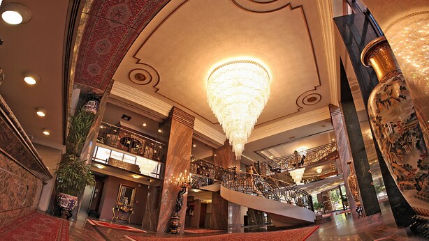A grand lobby with a large chandelier, marble columns, and a staircase. - Sabe Center Hotel (Asunción)