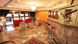 A hotel lobby with a red sofa, round tables, a bar area, and a patterned carpet. - Sabe Center Hotel (Asunción)