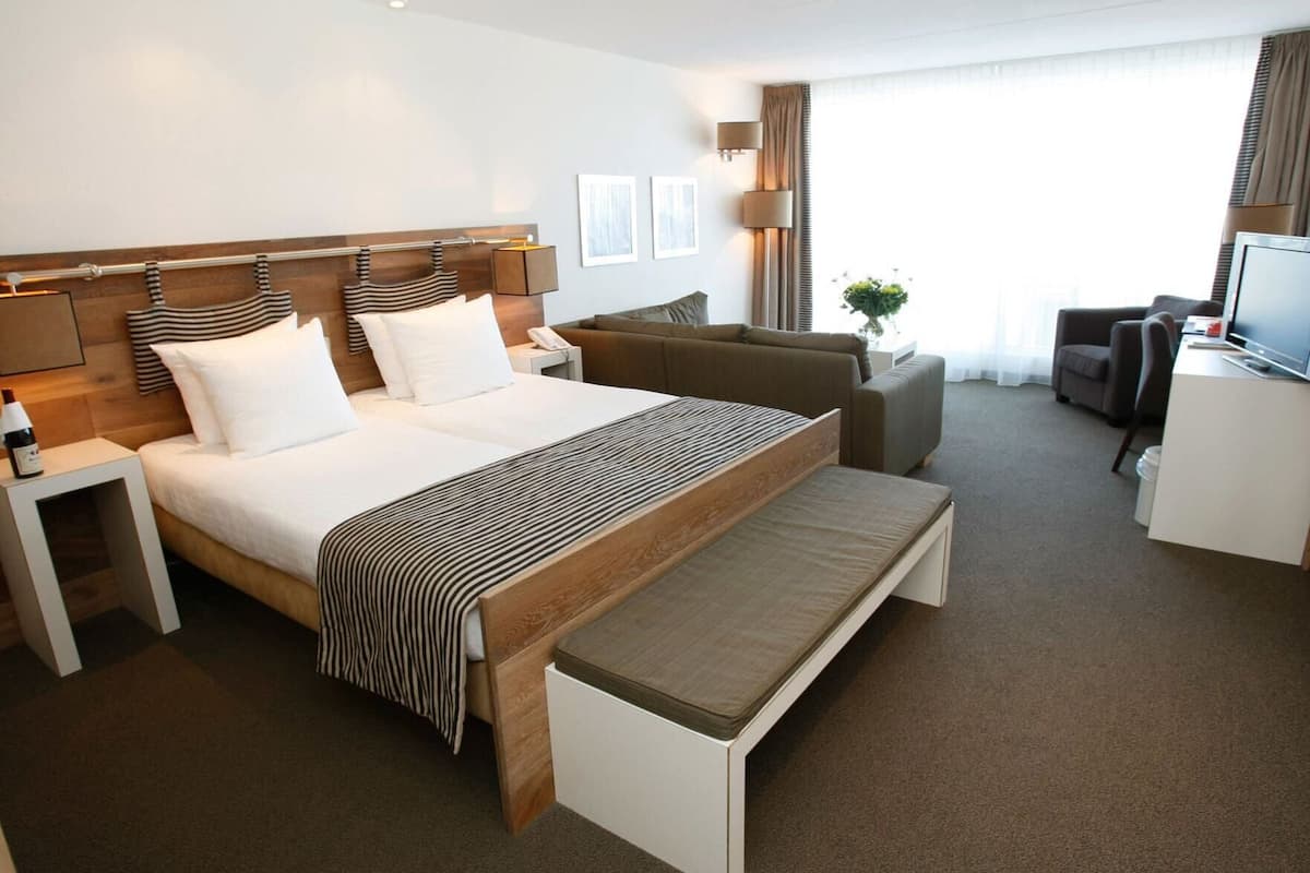 A hotel room with a large bed, a desk, a chair, a TV, and a window with curtains.