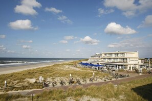A beachfront hotel with a large building, a sandy beach, and a grassy dune area.