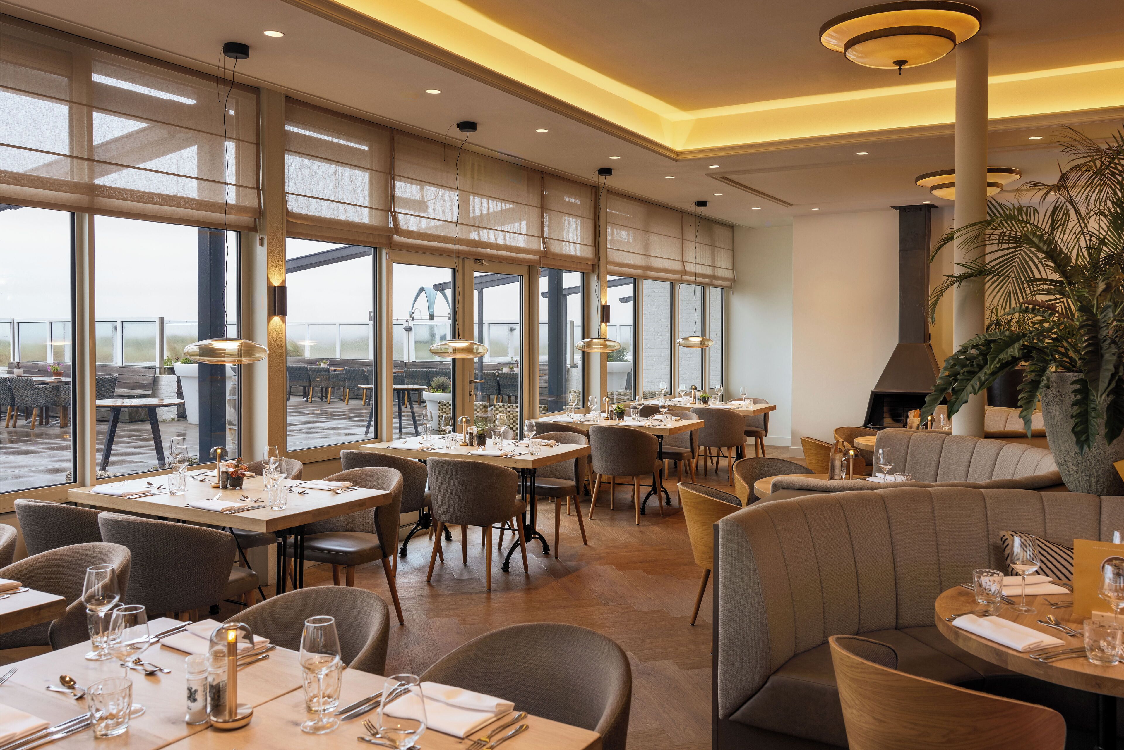 A spacious restaurant with large windows, multiple dining tables, and a variety of seating options.