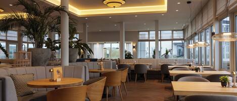 A modern restaurant interior with high ceilings, large windows, and a mix of seating options including tables and sofas.