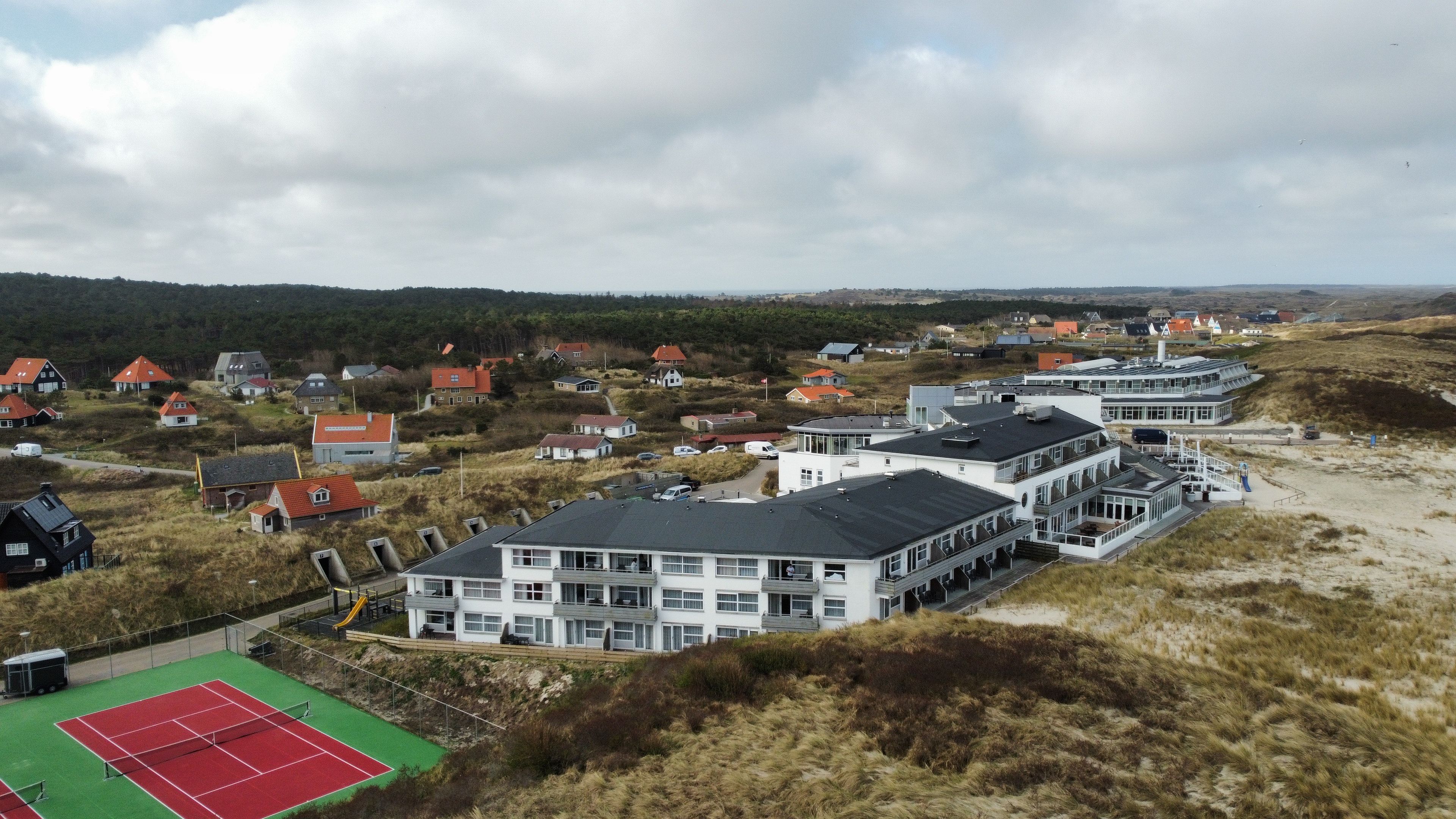 A coastal residential area with houses, a tennis court, and a large building with multiple floors.