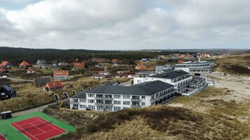 A coastal residential area with houses, a tennis court, and a large building with multiple floors.