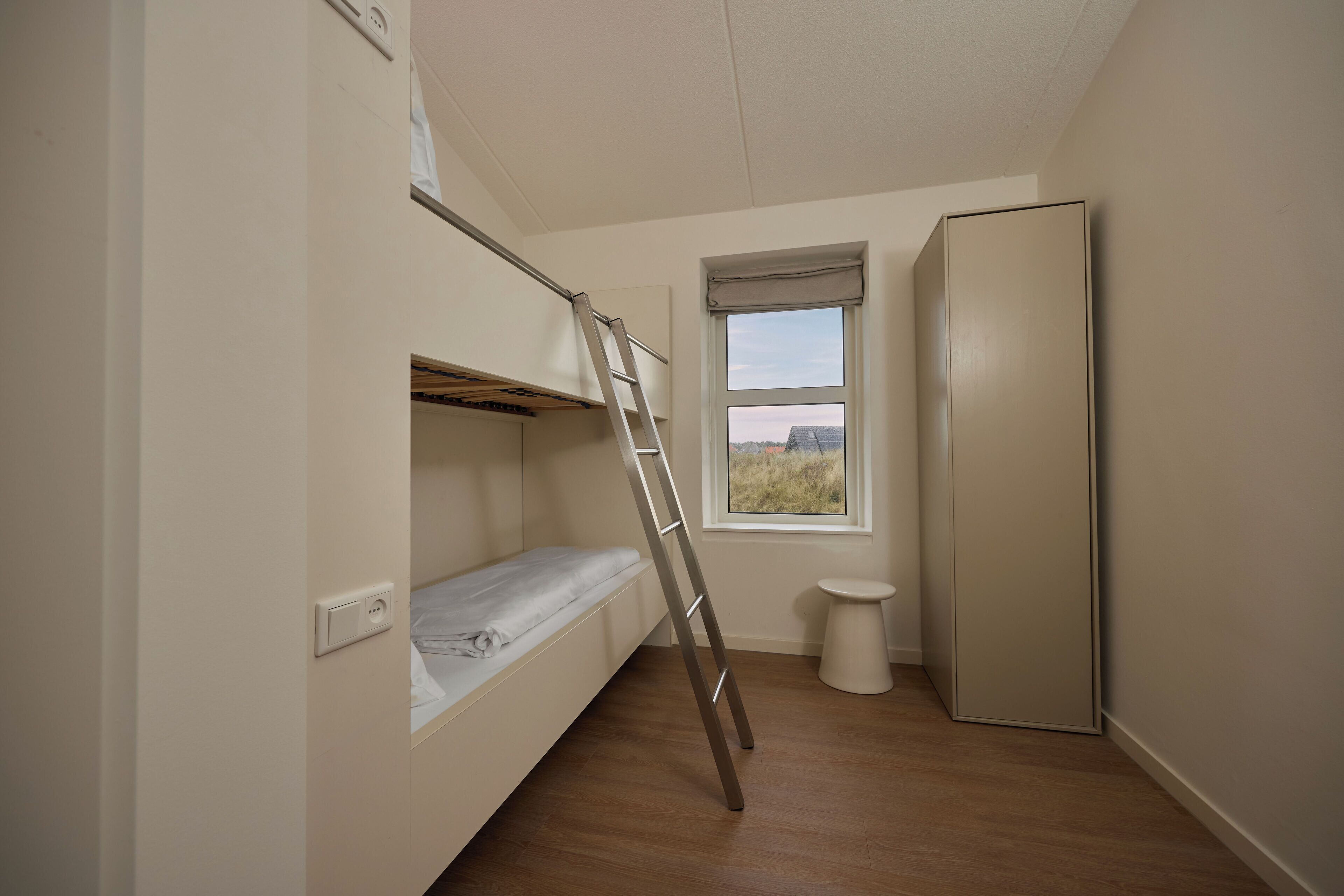 Een kleine, compacte kamer met een stapelbed, een trapje, een toilet en een koelkast.