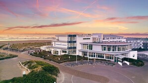 A modern hotel with a glass facade, located near a beach. - WestCord Strandhotel Seeduyn (Vlieland)