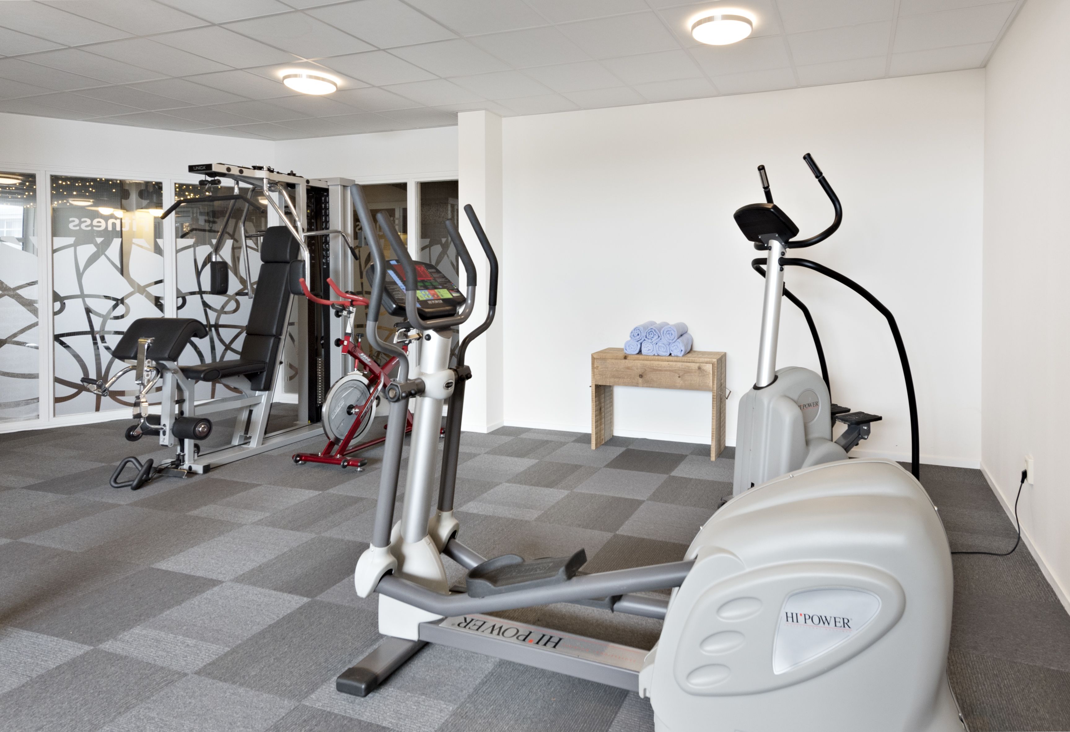 A gym with cardio machines, weight machines, and a small wooden table with dumbbells.