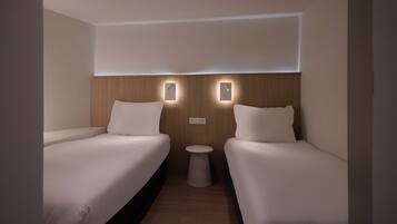 A hotel room with two single beds, a small round table, and wall-mounted lighting.
