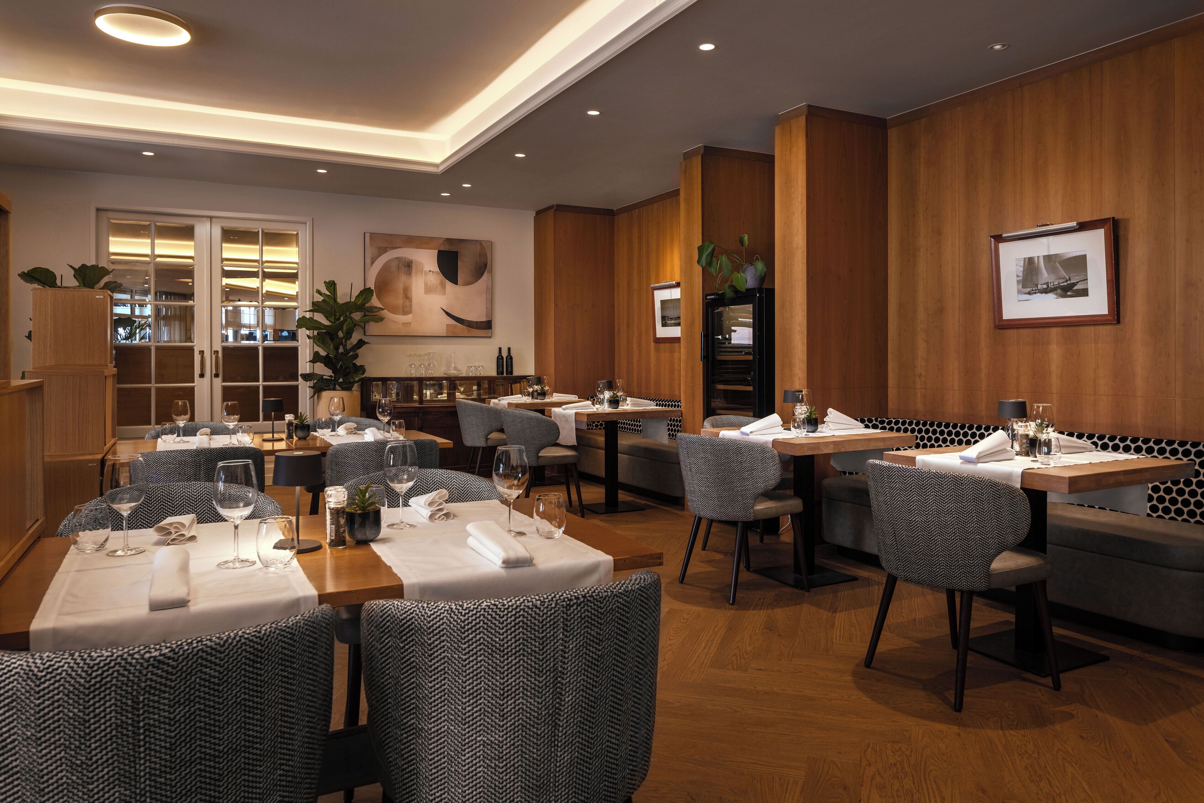Un restaurante con varias mesas y sillas, paneles de madera en las paredes y un cuadro abstracto grande.