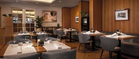 Un restaurante con varias mesas y sillas, paneles de madera en las paredes y un cuadro abstracto grande.