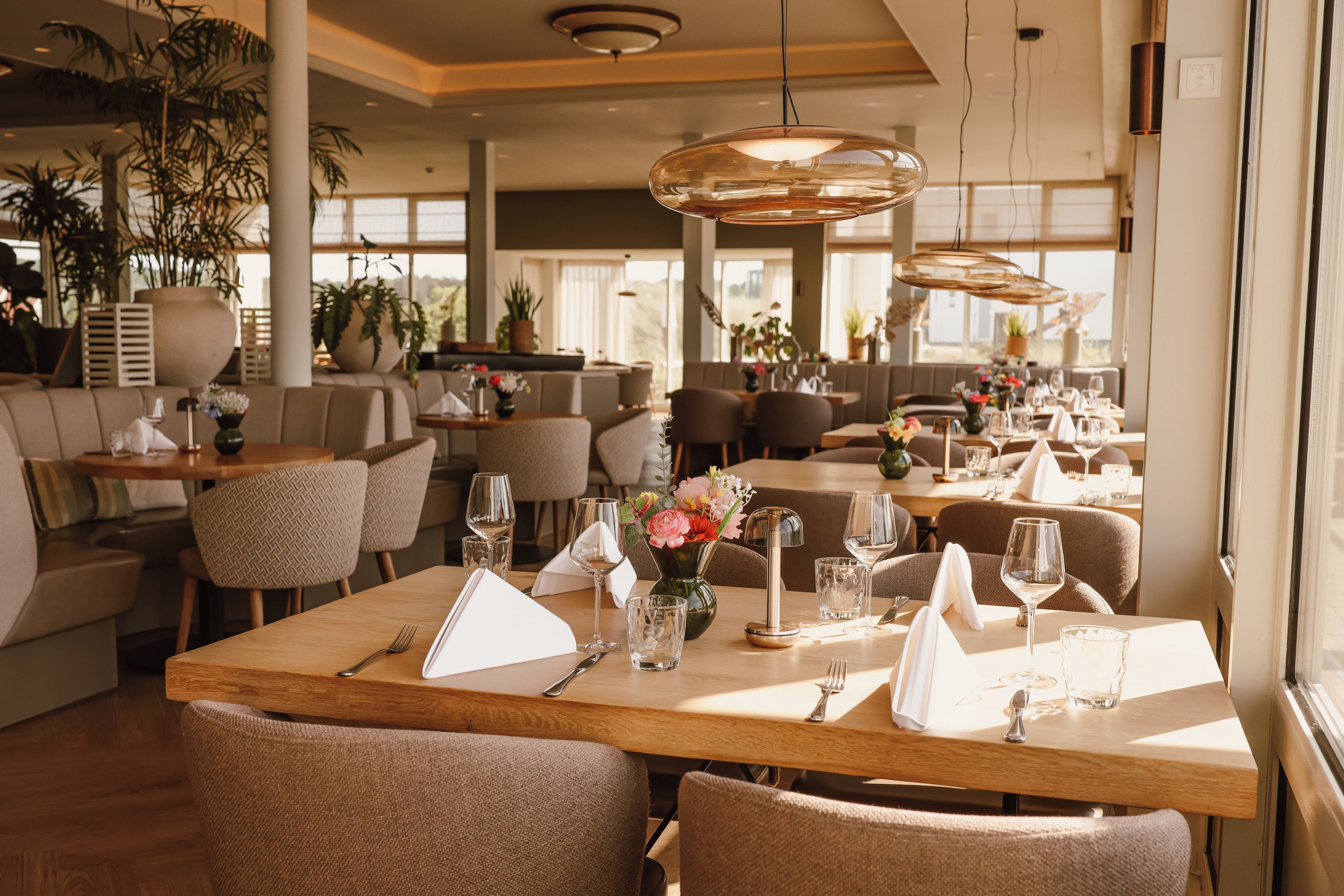 A restaurant interior with wooden tables, chairs, and hanging pendant lights.