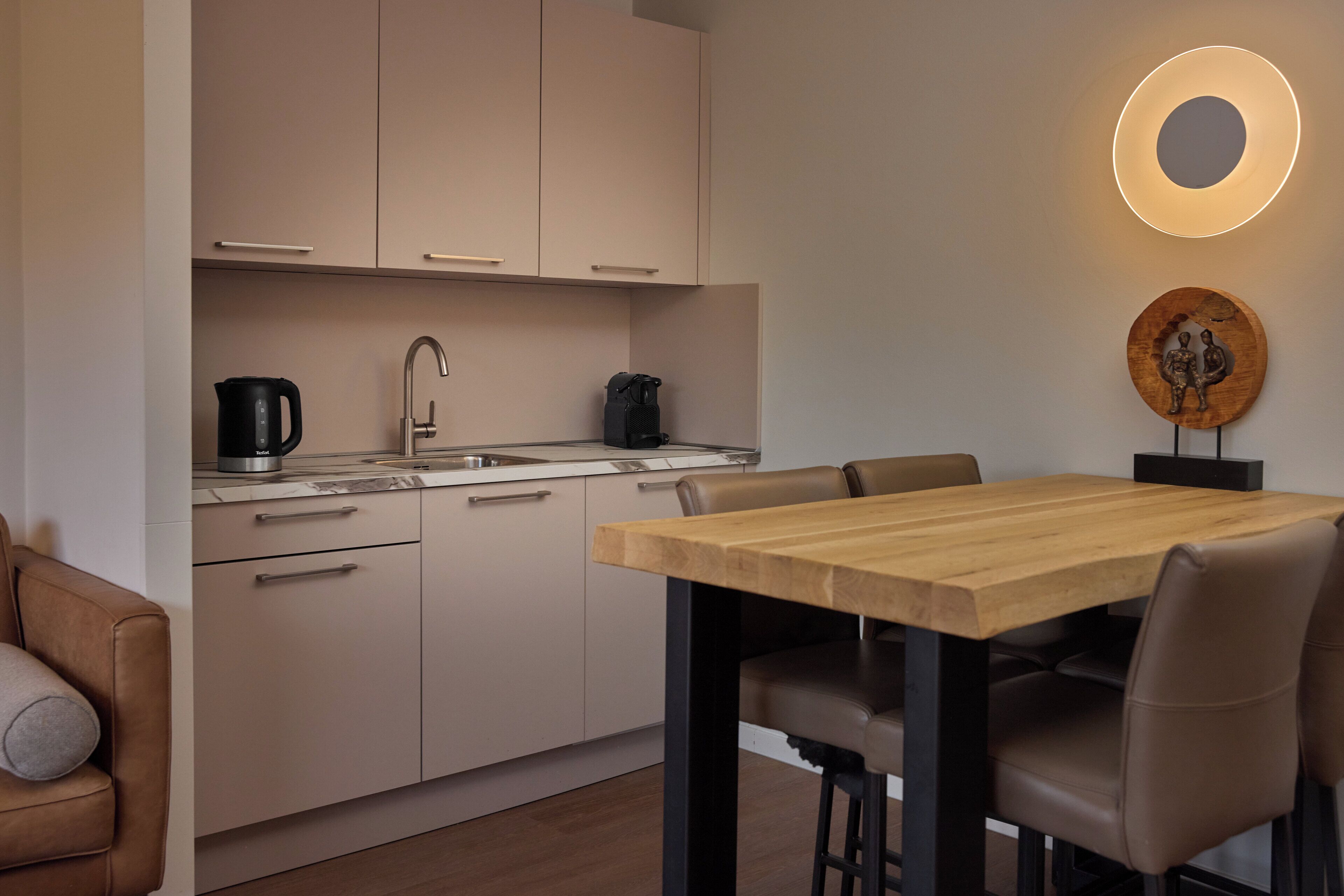 Une cuisine moderne avec une table et des chaises en bois, une bouilloire et une machine à café.