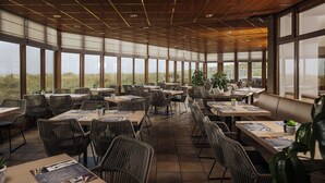 A spacious outdoor dining area with large windows, wicker chairs, and tables set for dining. - WestCord Strandhotel Seeduyn (Vlieland)