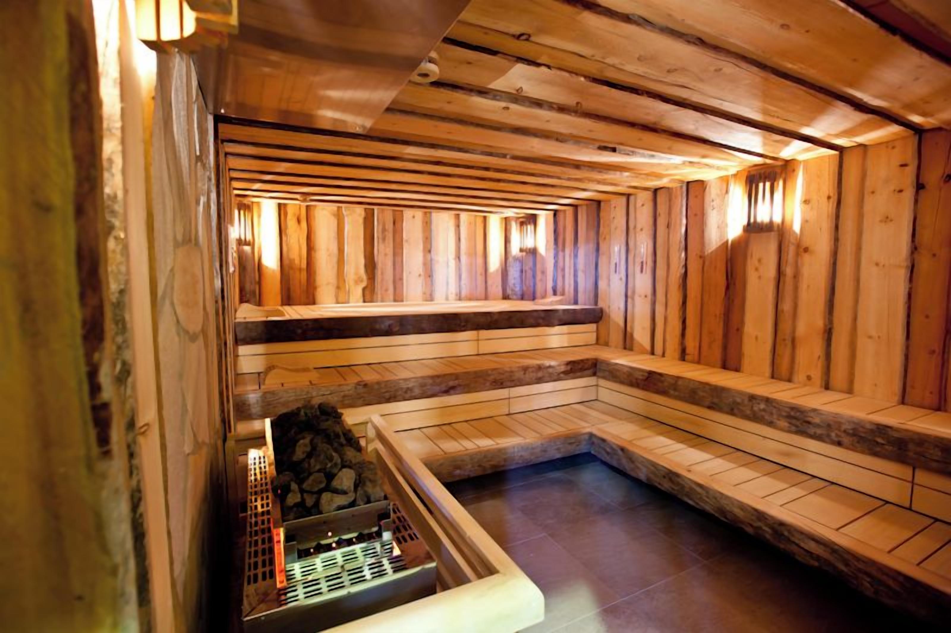 Una sauna con bancos de madera y un banco de piedra, un calentador de piedra y paredes de madera.
