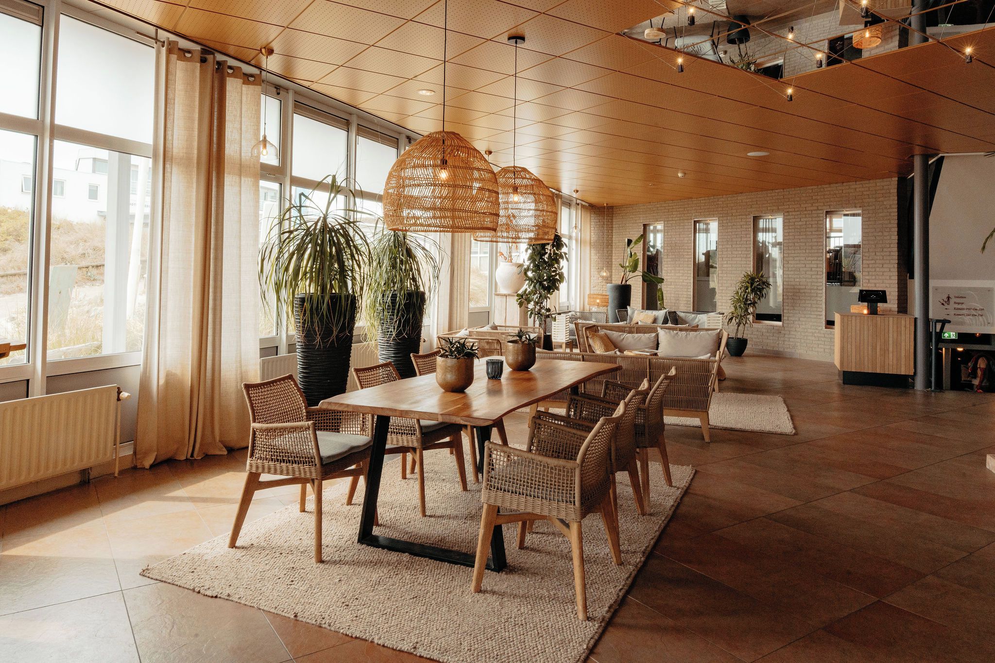 A spacious room with a large wooden table, wicker chairs, and hanging rattan lamps.