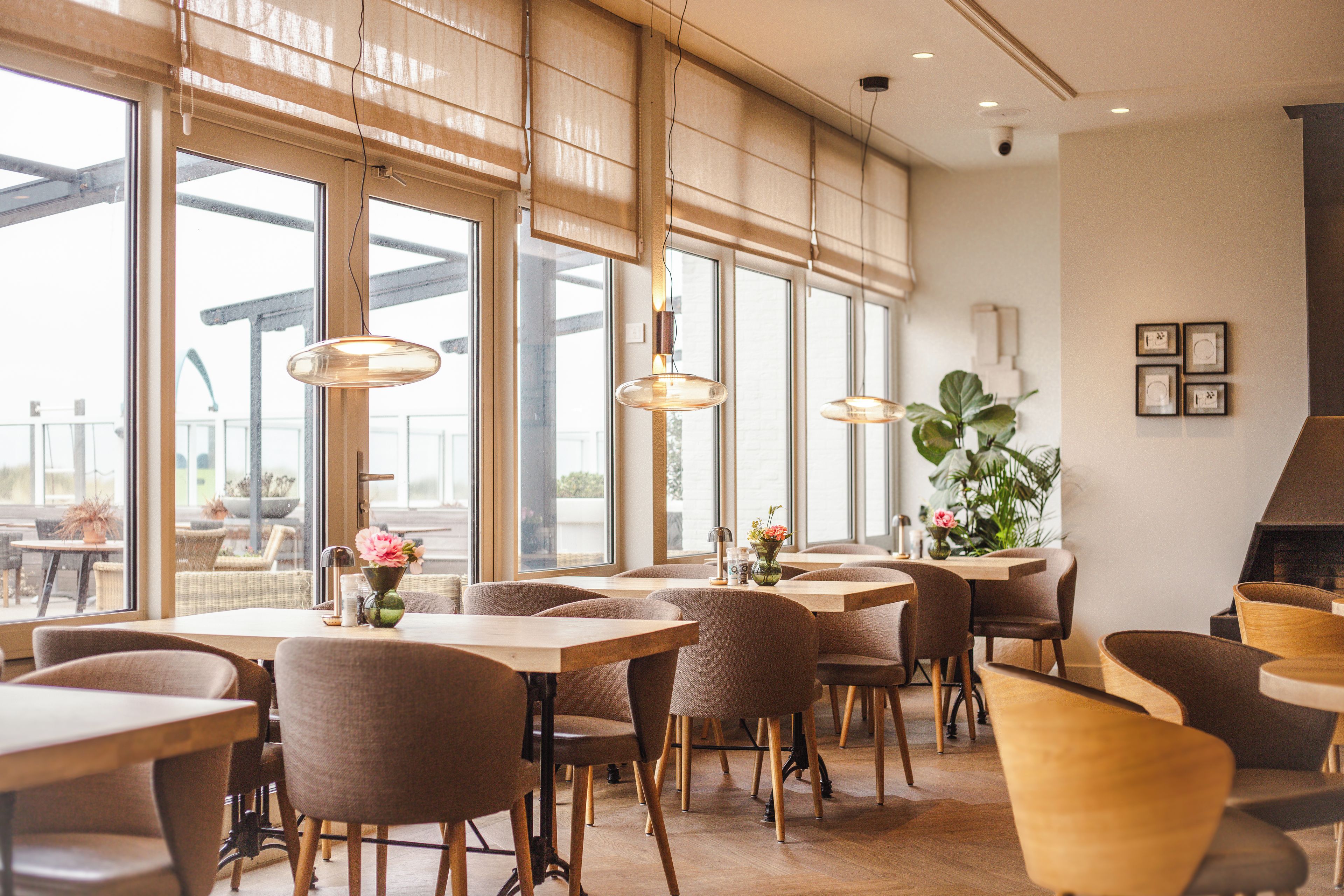Ein Restaurantinneres mit großen Fenstern, Holztischen und -stühlen.