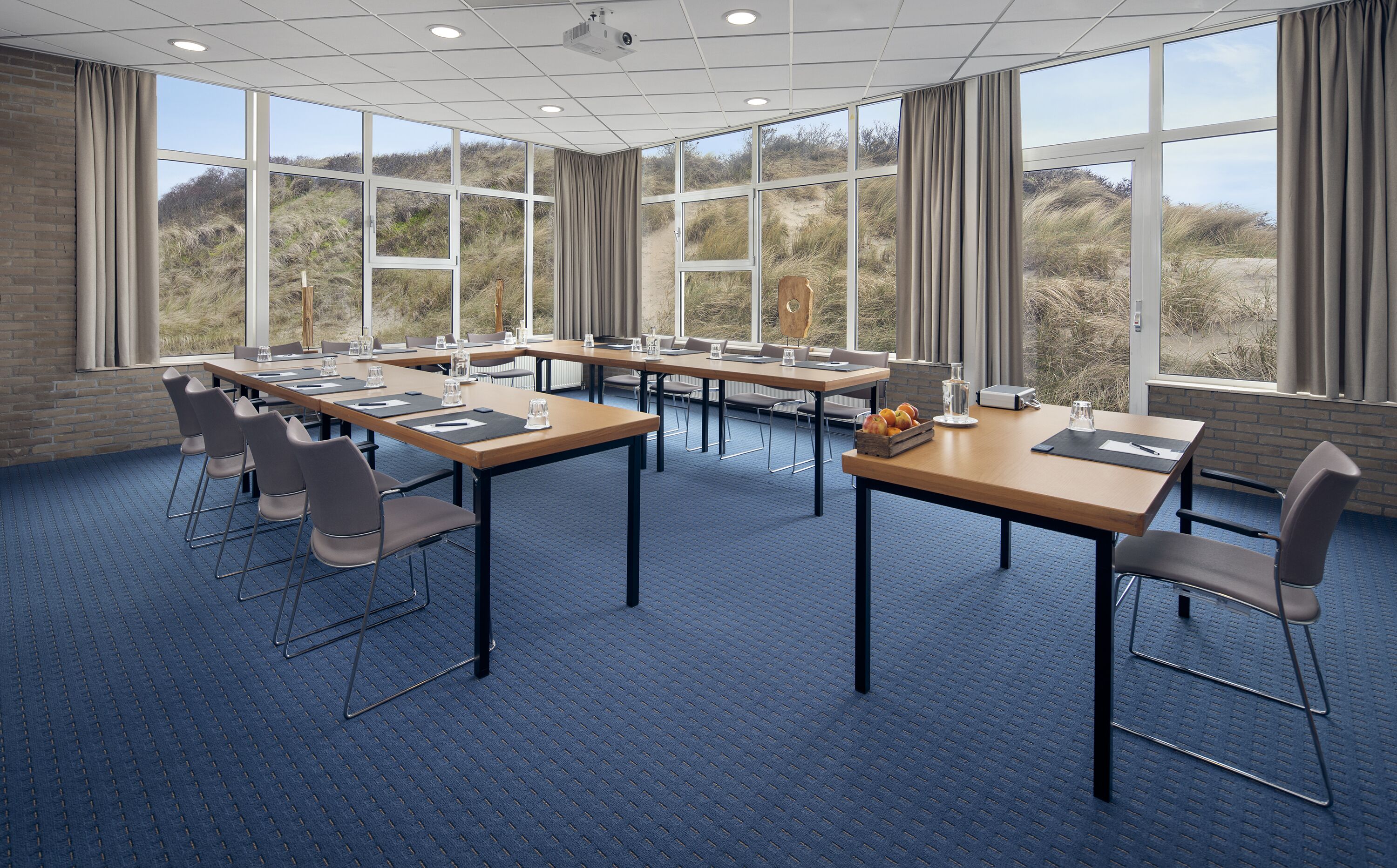 Un salón de conferencias con ventanas amplias, alfombra azul y mobiliario moderno.