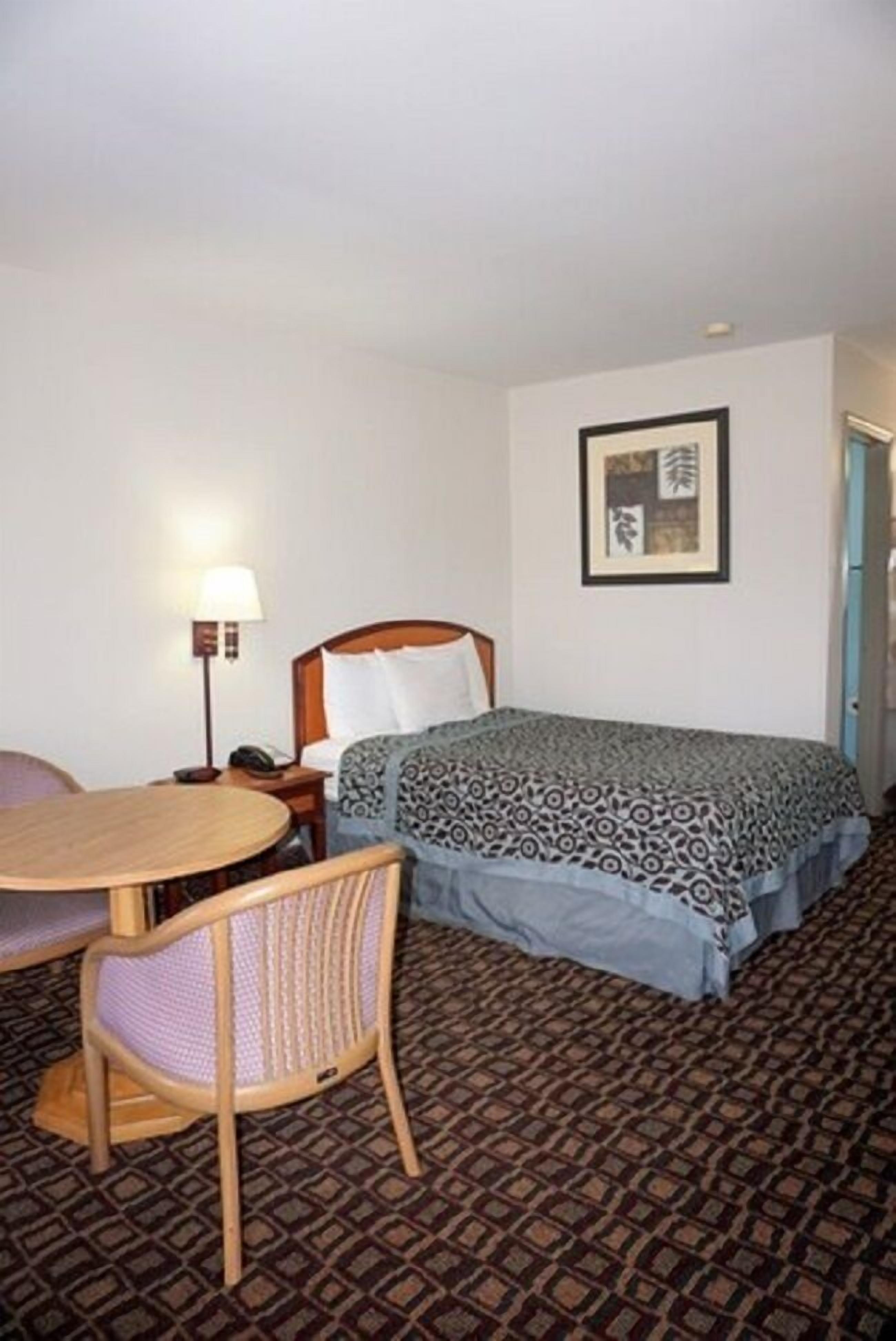 A hotel room with a bed, a chair, a table, and a lamp.