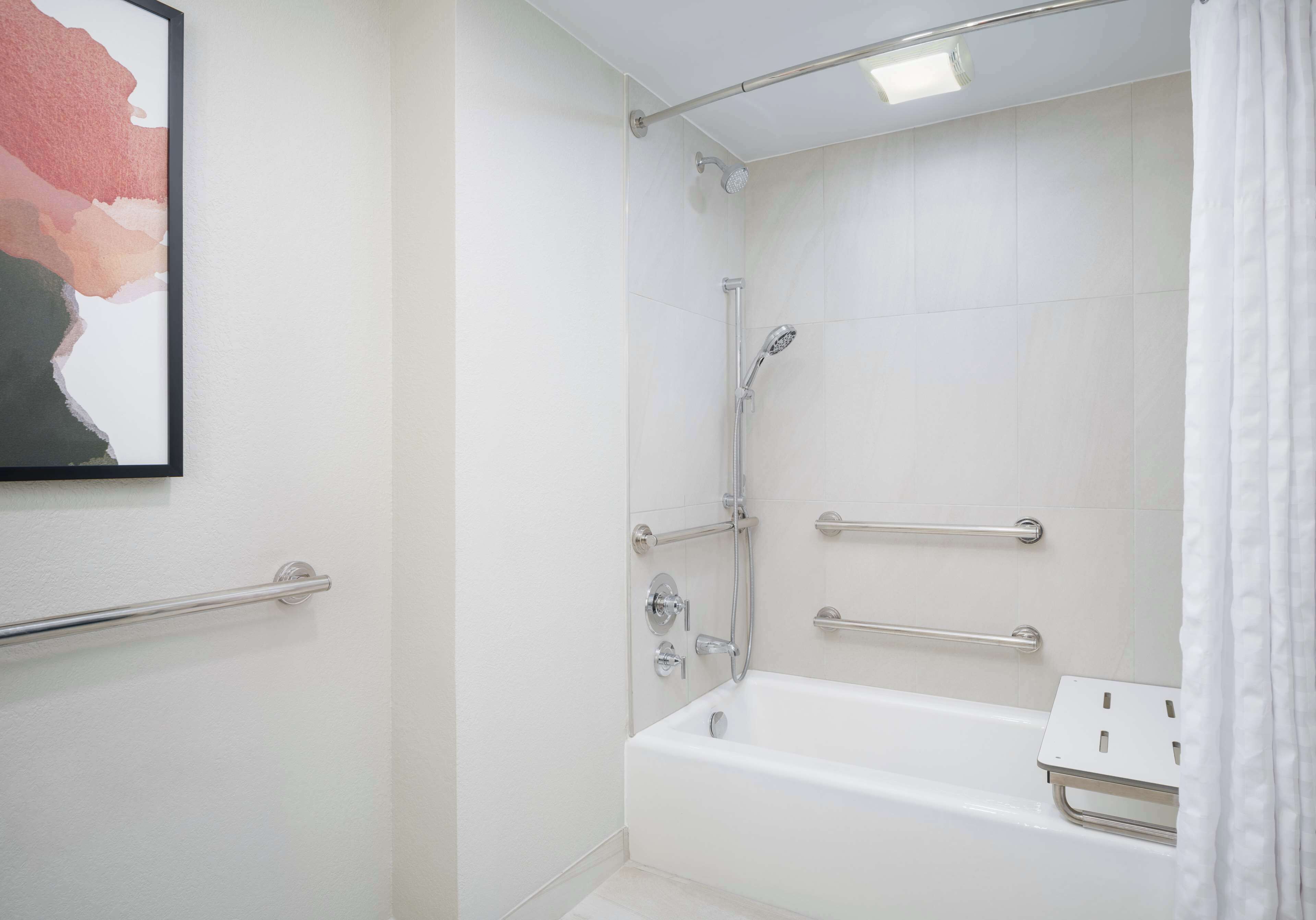 Ein modernes Badezimmer mit bodengleicher Dusche, Haltegriffen und einer weißen Badewanne.