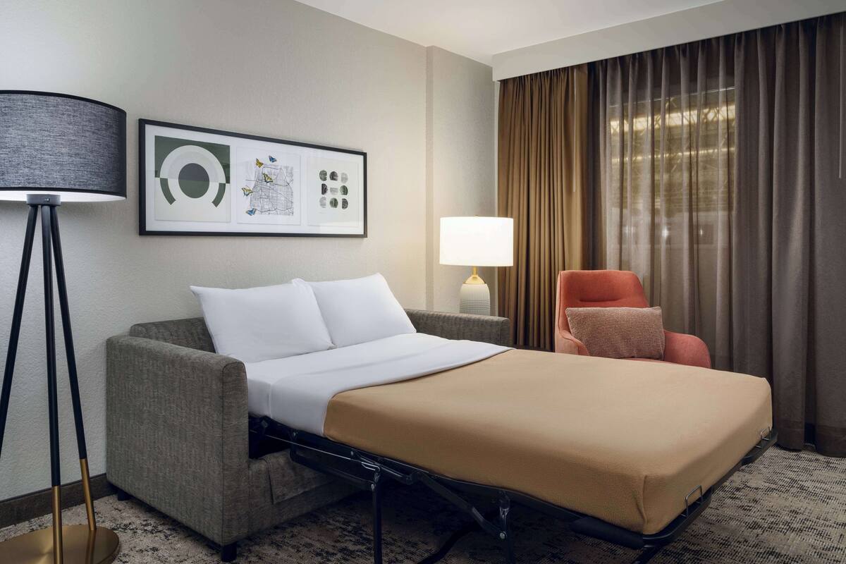 A hotel room with a bed, a sofa, a lamp, and a chair.