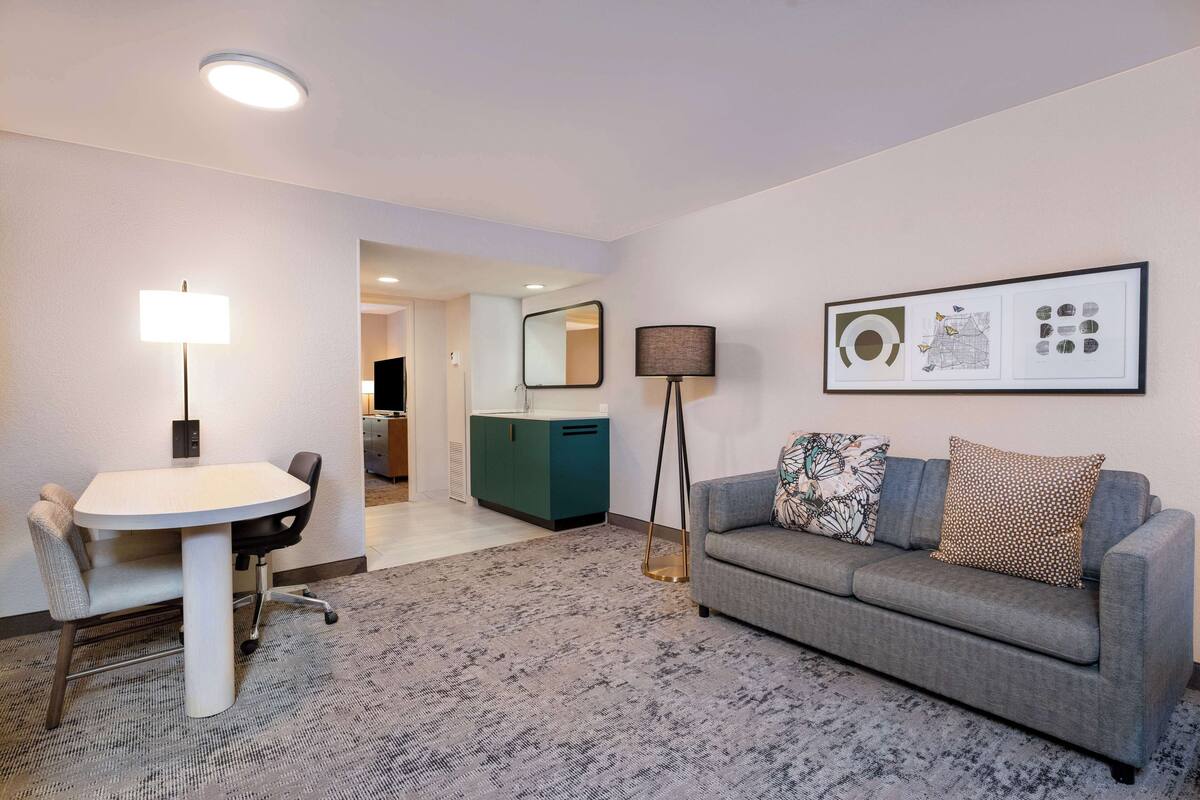 A modern living room with a gray sofa, a white dining table, and a floor lamp.