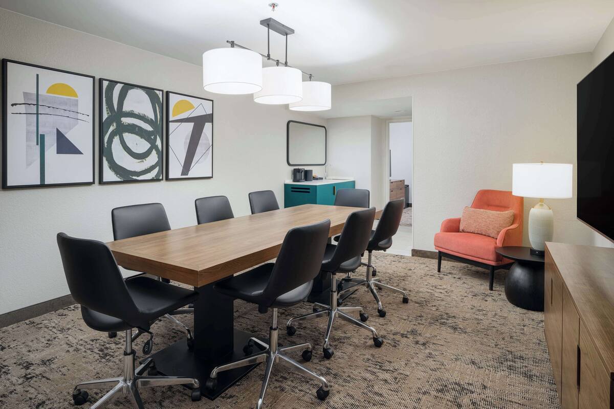 A conference room with a wooden table, black chairs, a teal accent wall, and abstract artwork.