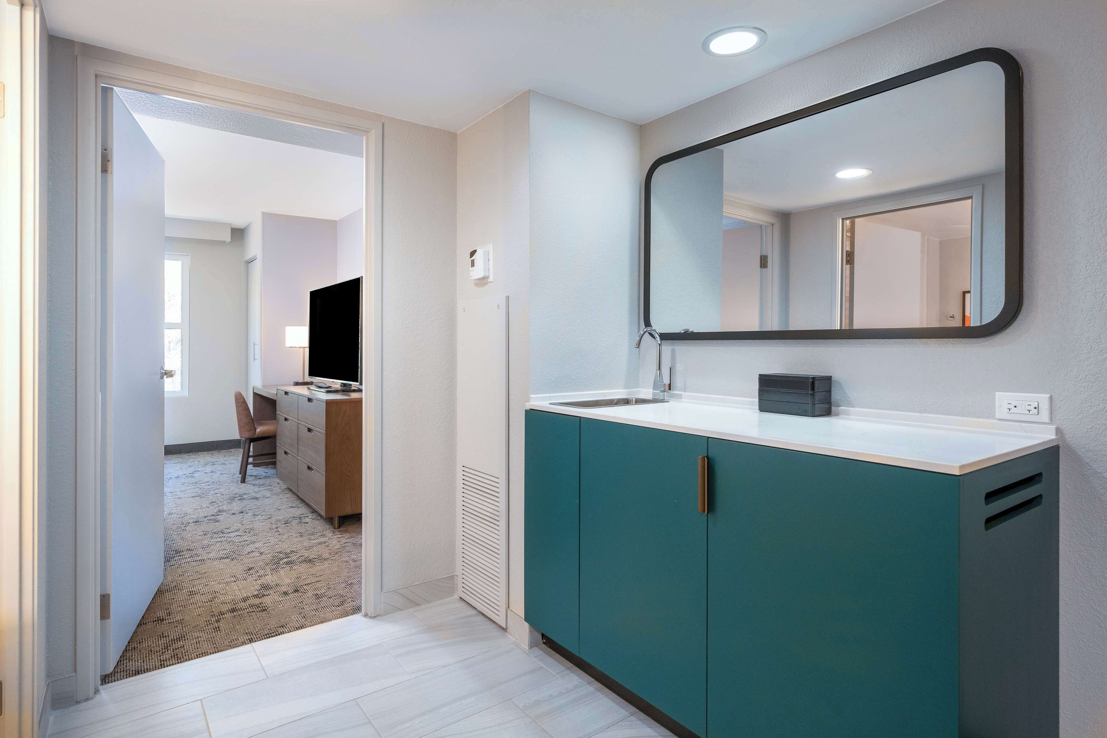 A modern bathroom with teal cabinets, a white countertop, and a large mirror.
