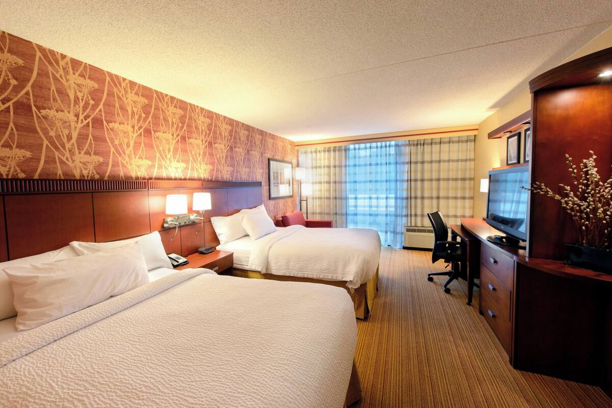 A hotel room with two beds, a desk with a television, and a large window with curtains.