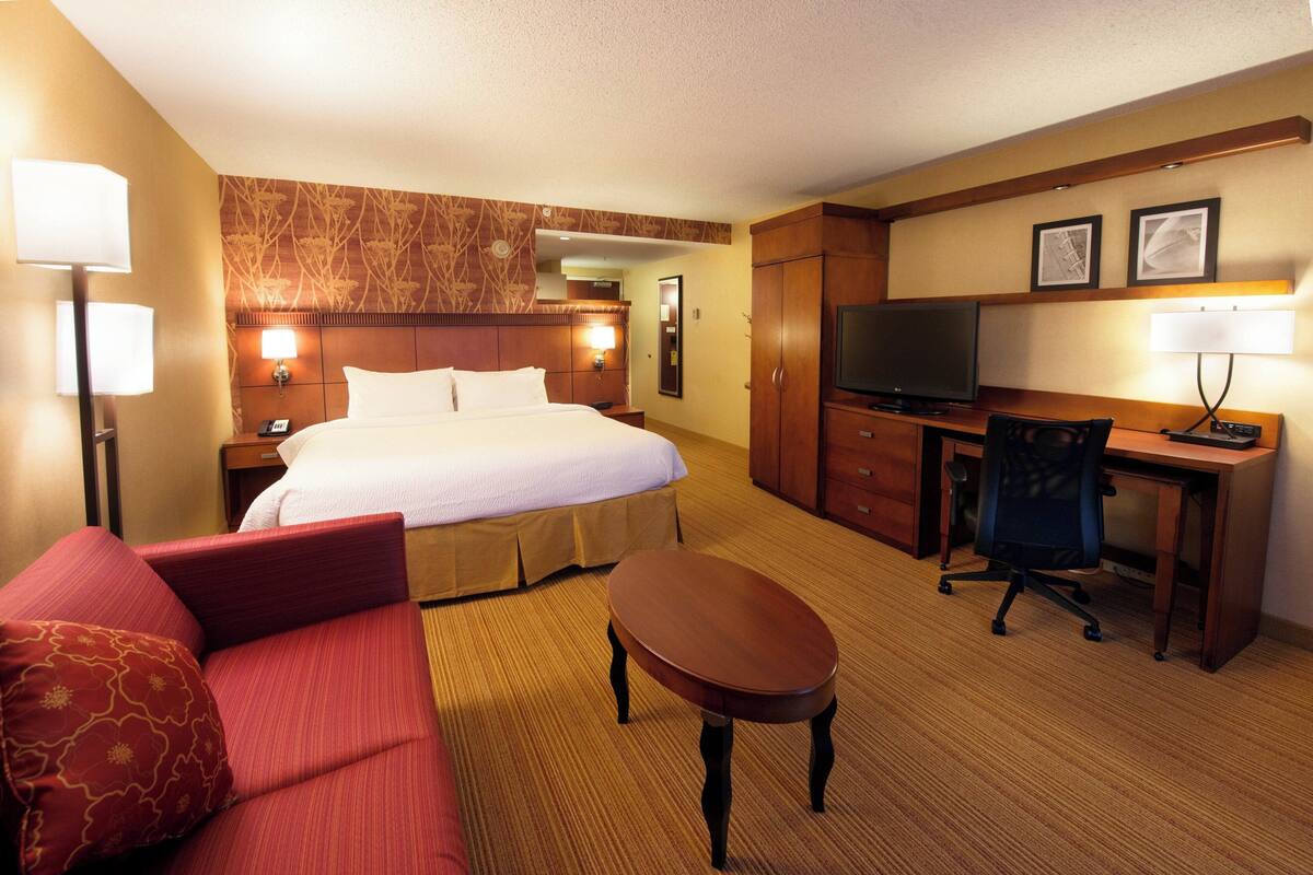 A hotel room with a bed, a desk, a chair, a TV, and a sofa.