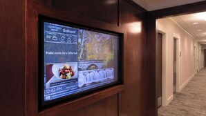 Pantalla digital en un pasillo que muestra un pronóstico del tiempo, el menú de un restaurante y una marca de tiempo.