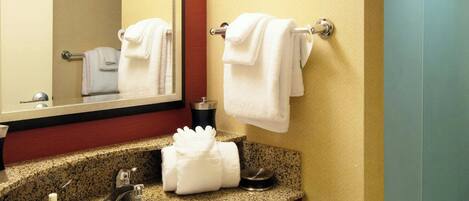 Baño de hotel con lavamanos de encimera de granito, un espejo y un perchero para toallas.