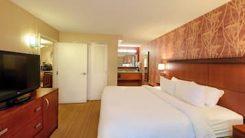 A hotel room with a bed, a TV on a wooden cabinet, a bathroom with a mirror, and a wall with a floral pattern.