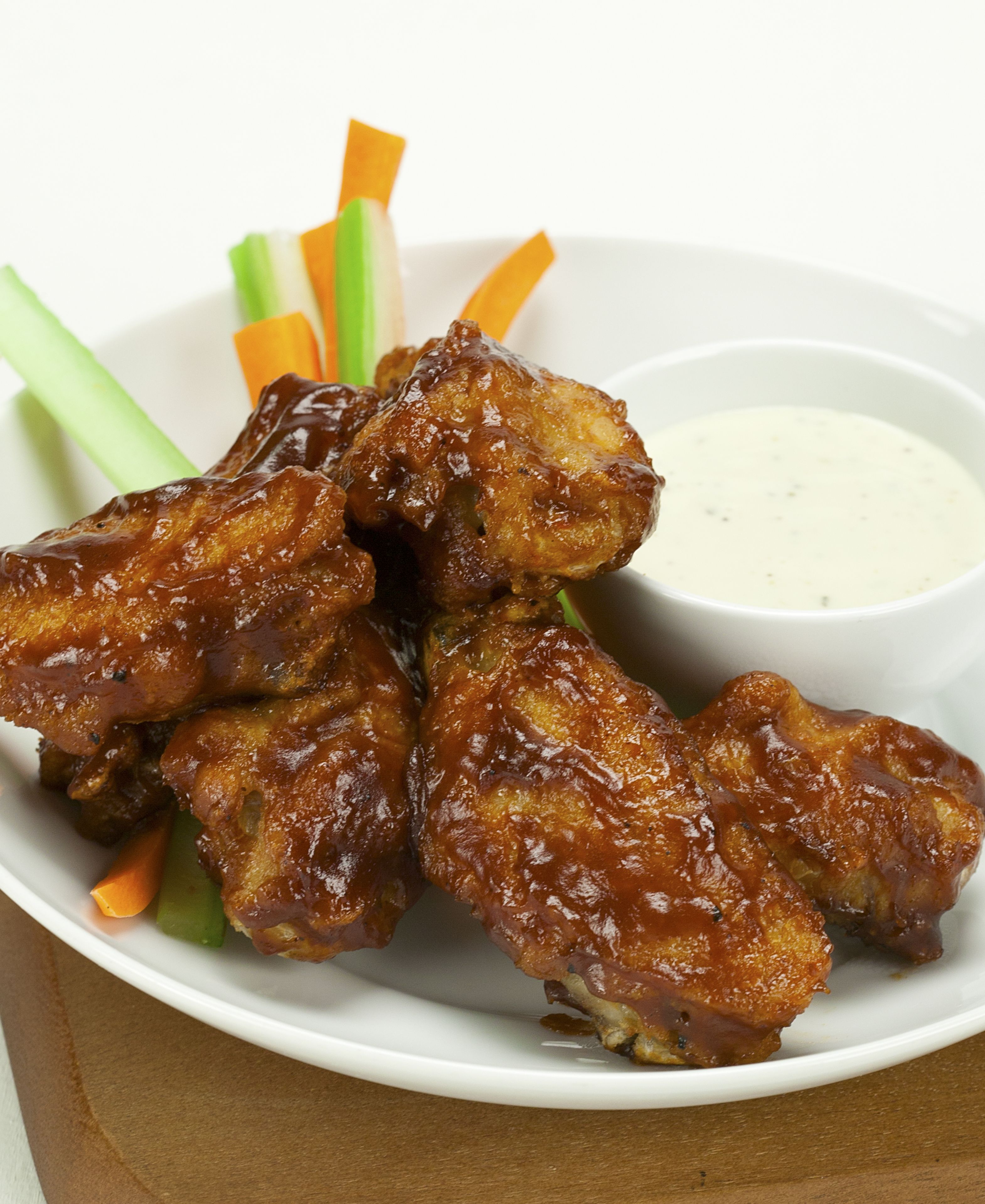 A plate of chicken wings with celery sticks and a small bowl of sauce.