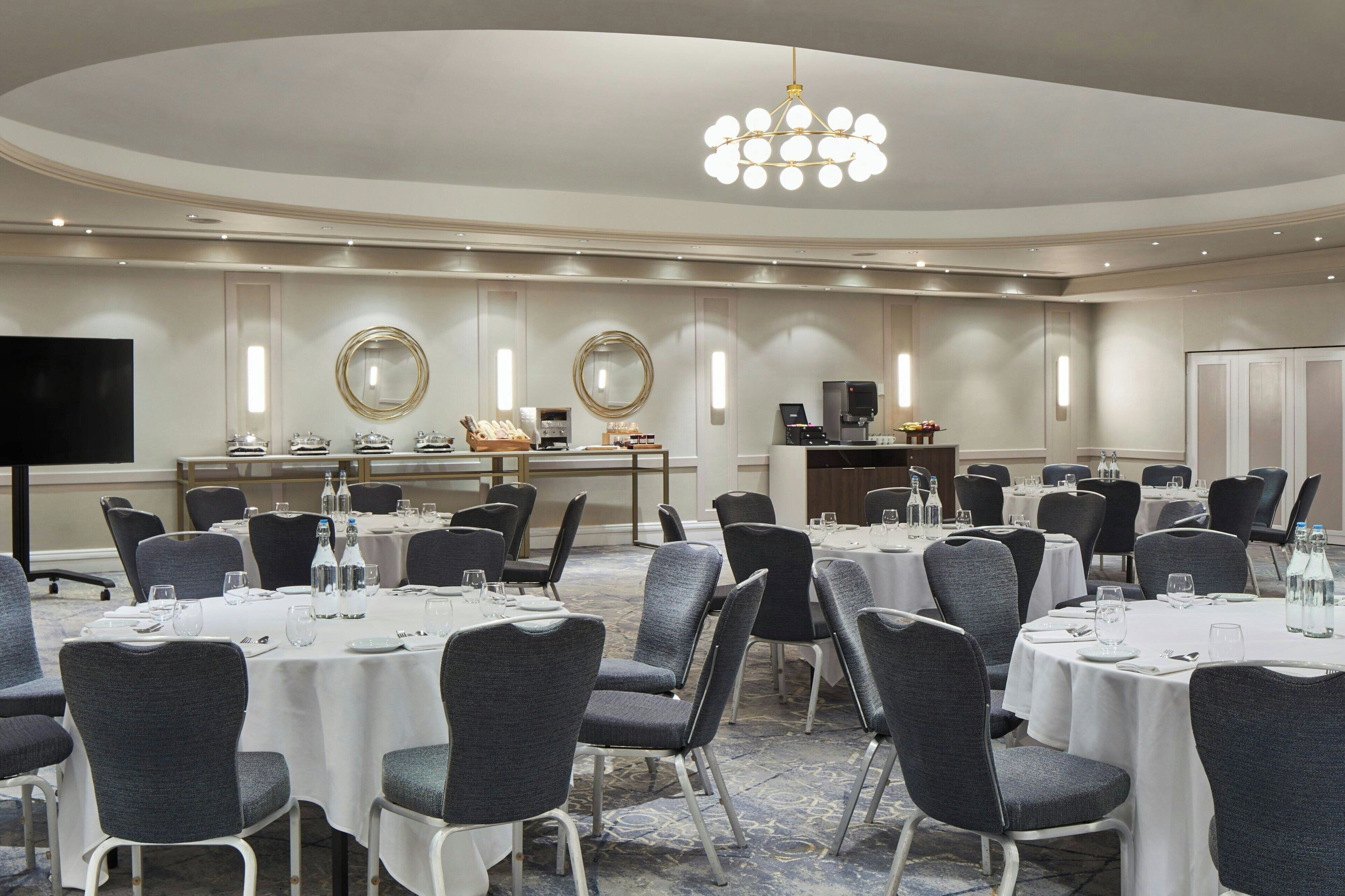 A conference room with round tables, chairs, and a large screen.