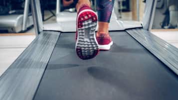 Un primo piano di un tapis roulant con i piedi di una persona in scarpe da corsa.