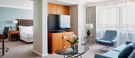 Une chambre d’hôtel moderne équipée d’un lit, d’une télévision, d’un canapé, d’une table basse et offrant une vue sur la ville grâce à de grandes fenêtres.