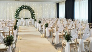 A formal event space with rows of chairs, a carpeted aisle, and a floral arch.