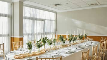 A long dining table set for a formal event with chairs, candles, and floral centerpieces.