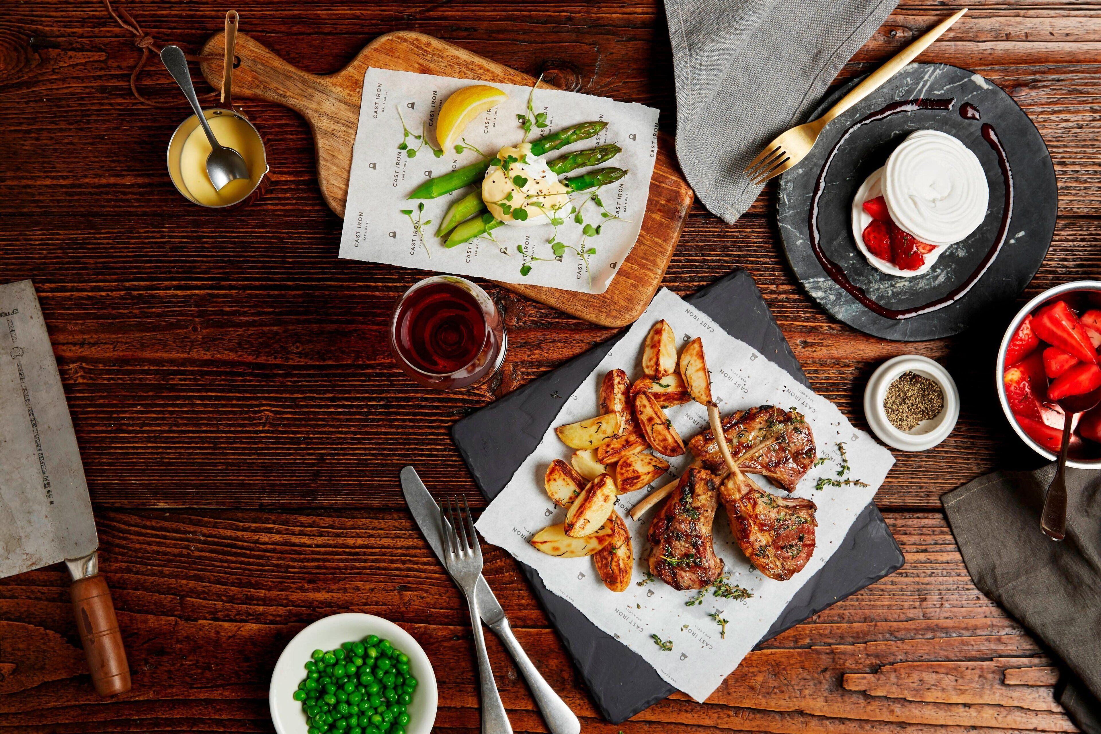Une table en bois sur laquelle on trouve une variété de plats, notamment des pommes de terre rôties, des asperges et un steak accompagné d’une portion de petits pois.