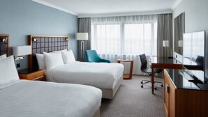 A hotel room with two beds, a desk, a chair, a TV, and a window with curtains.
