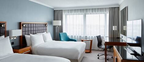 A hotel room with two beds, a desk, a chair, a TV, and a window with curtains.