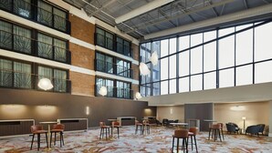 A spacious indoor area with multiple seating arrangements, large windows, and a high ceiling.