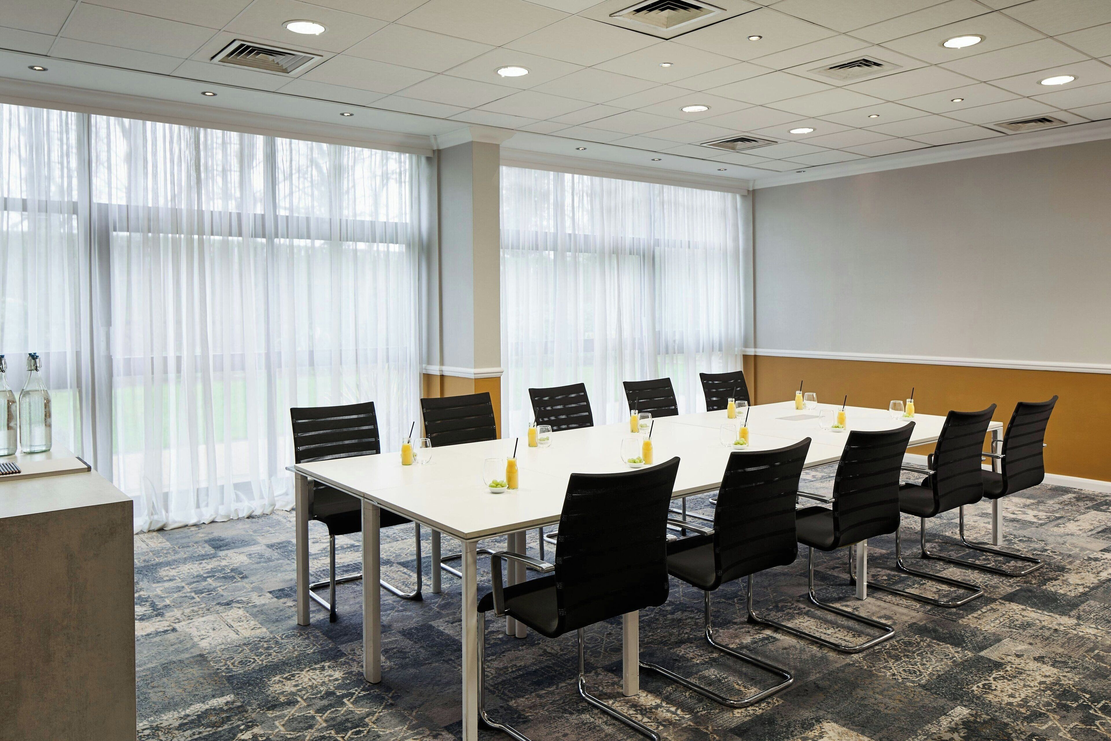 A conference room with a long table, black chairs, and a carpeted floor.