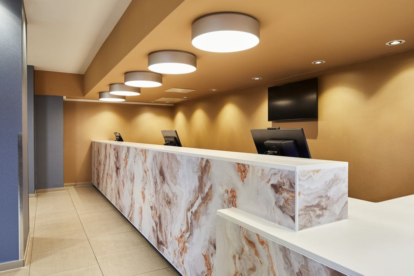 A reception desk with a marble design, multiple light fixtures, and a flat-screen TV on the wall.