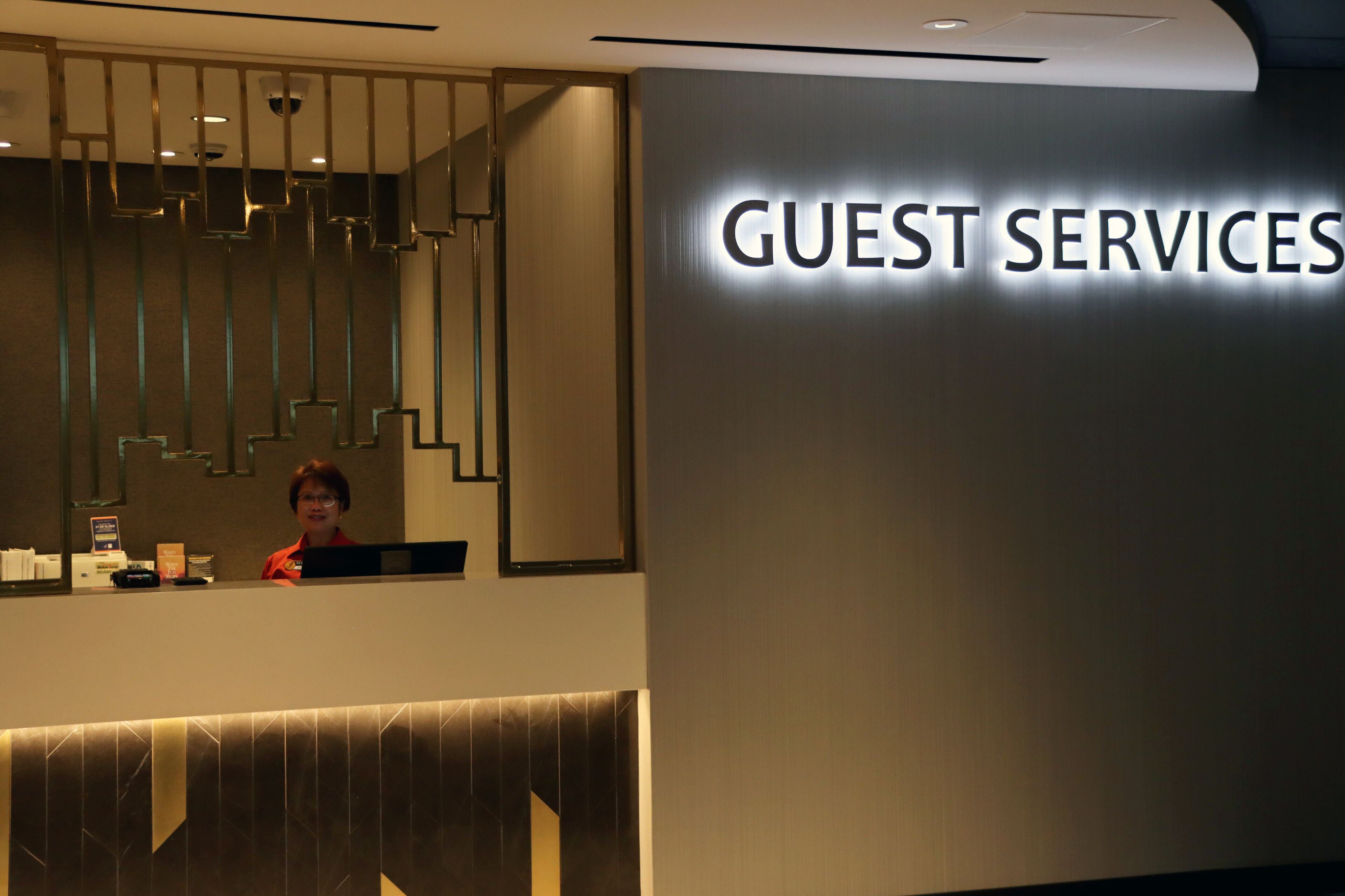 Ein Empfangstresen mit einem Schild, das "GUEST SERVICES" zeigt, und einem modernen Innendesign.